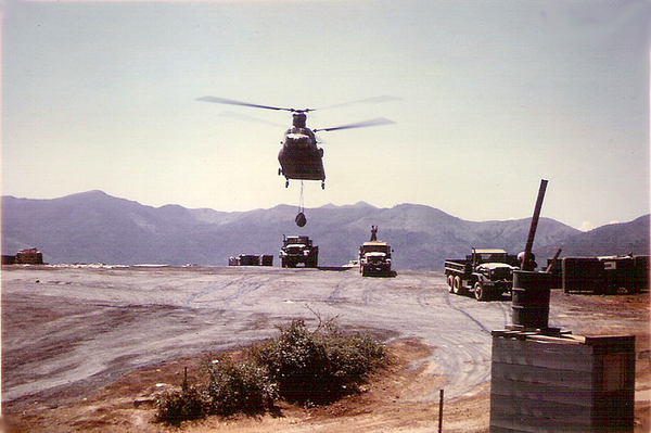 Helo Loading Area - LZ English
Next to our bunker was this helicopter loading area.  It was oiled to keep the dust down.  Here a Chinook is picking up a load of ammo, going to one of the firing batteries.  Man atop truck is giving signals to the pilot.  Foreground: Bn Commander LTC Bobzien's hot water shower.

