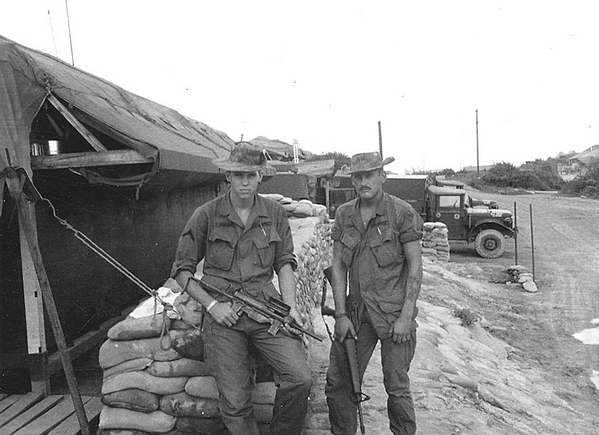 Commo Dudes: Ready for anything
The Duc Pho hill was off to the far right- out of the photo. These HQ battery commo fellows were PFC Hogan (left) and Sgt. Trainor. They were purposely looking tough here. We managed to somehow acquire a large stash of unusual "unauthorized" firearms (I had a bunch of them) and the PFC is holding what we fondly referred to as a "grease gun".  The sarge was out of Texas as I recall. 

