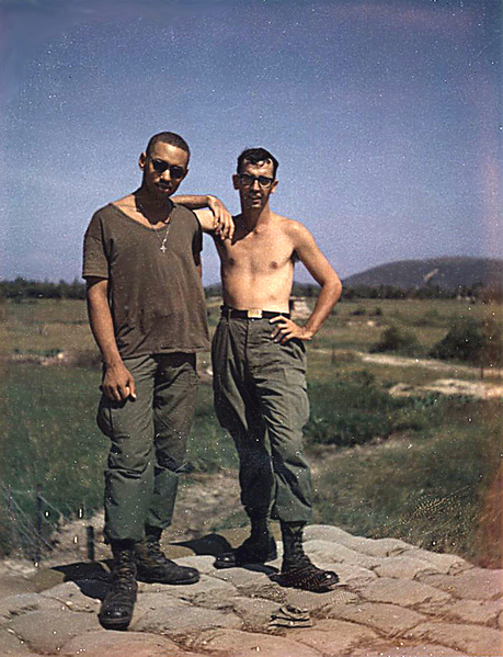 Downed Chopper
Off in the background of this shot is a rice paddy with a Huey helicopter laying upside-down in it. Guys who stood guard on this part of the Montezuma perimeter will recall the downed chopper. As far as I know, it was booby trapped and never recovered. This is me and commo buddy "Philly" from Philadelphia standing on top of a bunker on the perimeter.

