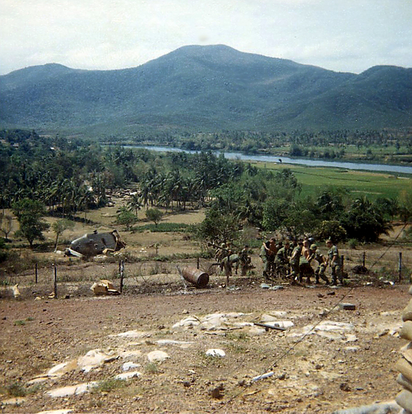 LZ English - Bong Son
(cont) Next thing I know, the Chinook crashes on its side and the guys inside are scrambling to get out! Here they are with the chopper in the background crashed and the guys trying to cross the perimeter barbed with to get back IN to LZ English! Some of them were scraped up pretty badly.

