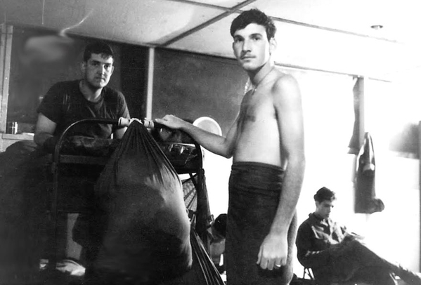 Sp4 David Jacobs, with towel, was the switchboard operator.  Mark Charters is reading a book over to the right.  The one on the upper bunk is UNK.  This area was the common hut.  Jesse White slept here also.  Anyone know the unknown soldier?
