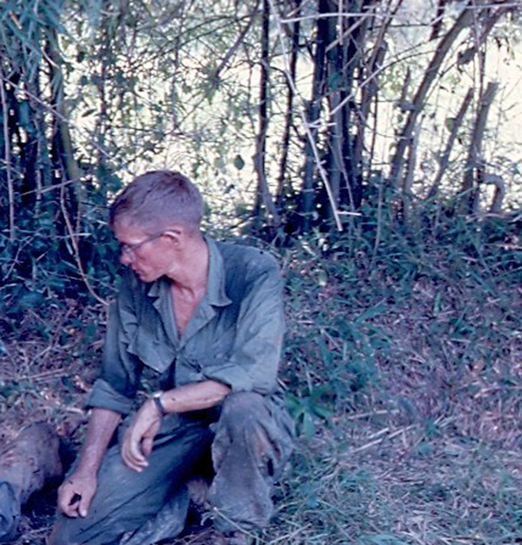 A very close call!
I'm kneeling on the ground next to a spider hole with a dead VC (not shown) laying next to me.  The infantry guys had thrown a hand grenade in the hole.  They thought that the VC was dead, so I stuck my head in the hole to take a look.  Based on what I described to the Infantry guys, they told me that the VC was not dead.  This created some excitement with my head looking down in the spider hole.  They threw a second hand grenade in the hole.  I figured out that the first grenade had wounded the VC so badly that he could not get his rifle, which I saw when I looked in the hole, in position to shoot me in the head.
