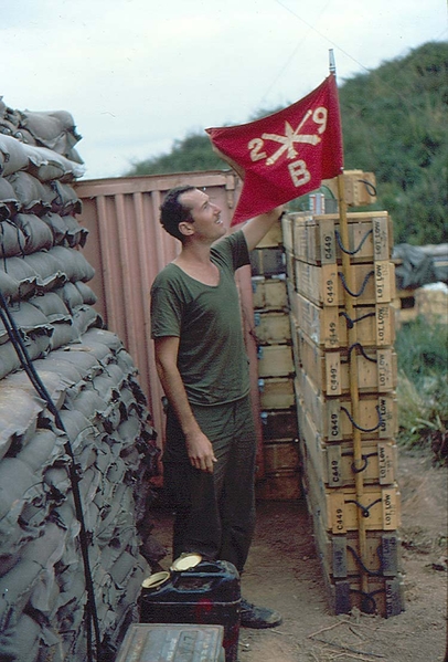 Showing the colors
Terry showing off the guidon of B/2/9 just outside the sandbagged CONEX, his "home away from home".
